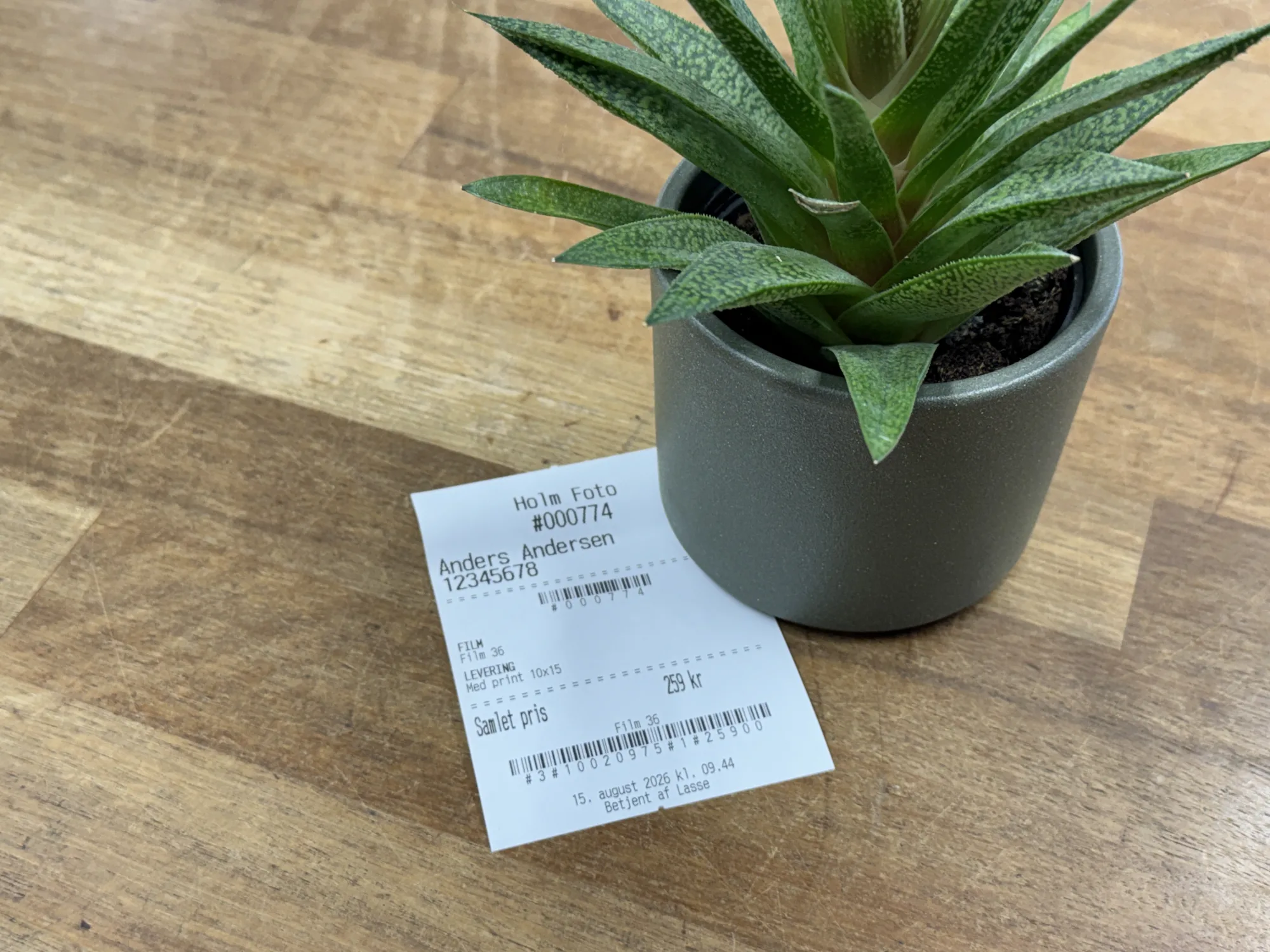 Kvitteringen udskrives direkte fra systemet via PrintNode til butikkens termoprinter.  Den indeholder ordrenummer, kundens navn og telefonnummer, en komplet specificeret oversigt over de valgte produkter og deres priser, opstartsgebyret samt det samlede beløb. Ved film- og negativordrer tilføjes der øverst en Code 128-stregkode med ordrenummeret, så laboratoriet kan scanne ordren direkte ind i deres workflow. Nederst genereres dynamiske C1st-stregkoder for hvert enkelt produkt. Medarbejderen scanner disse direkte ind i butikkens kassesystem, hvilket eliminerer behovet for manuelt at indtaste produkter og priser.